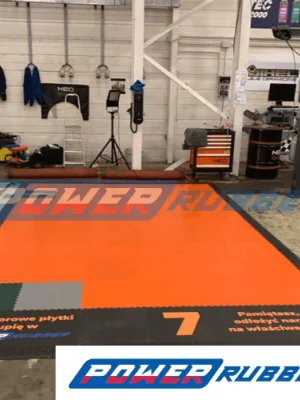 Pomarańczowe i czarne płytki PCV PowerFloor w garażu z podnośnikiem i kanałem samochodowym, odporna na olej, smary i nacisk punktowy, montaż w systemie puzzle4